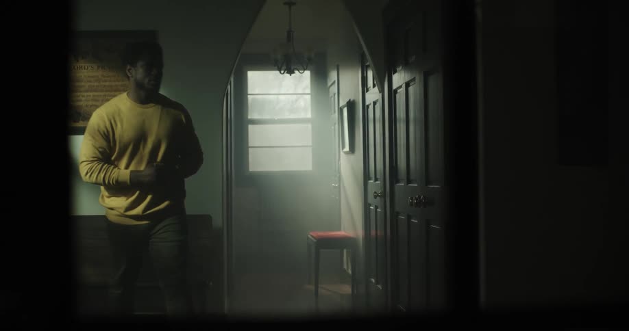 A man sitting down in a room then gets up and walks into another room