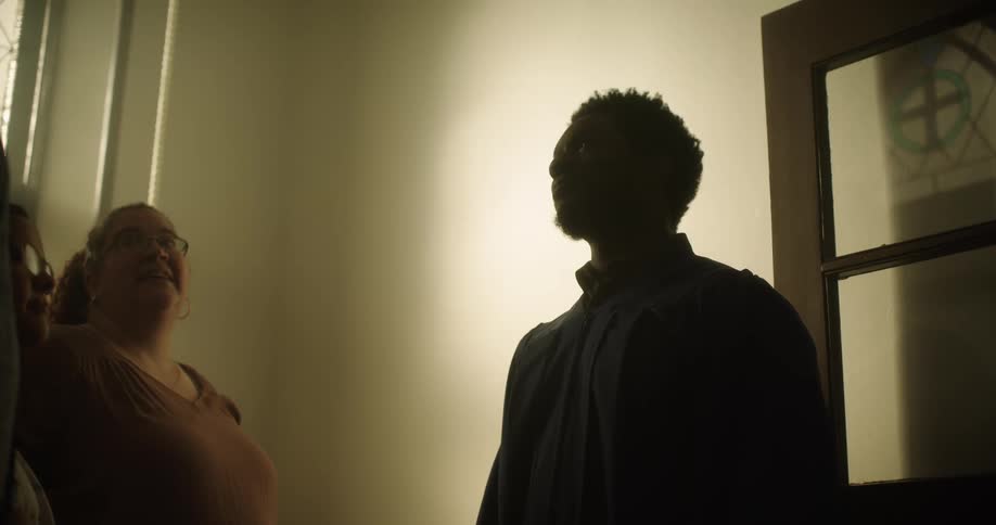 A black man stands in a church and talks with other members
