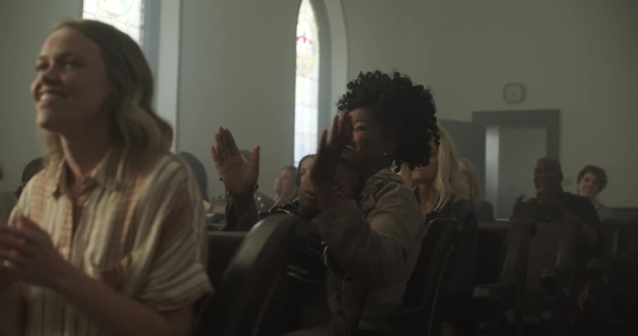 People sitting in church pews smile as they clap and sway in their seats