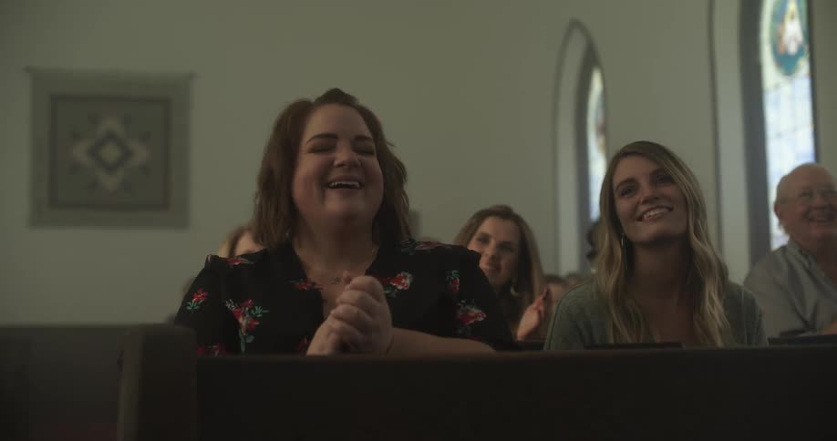 People sitting in church pews clap and smile and sway during service