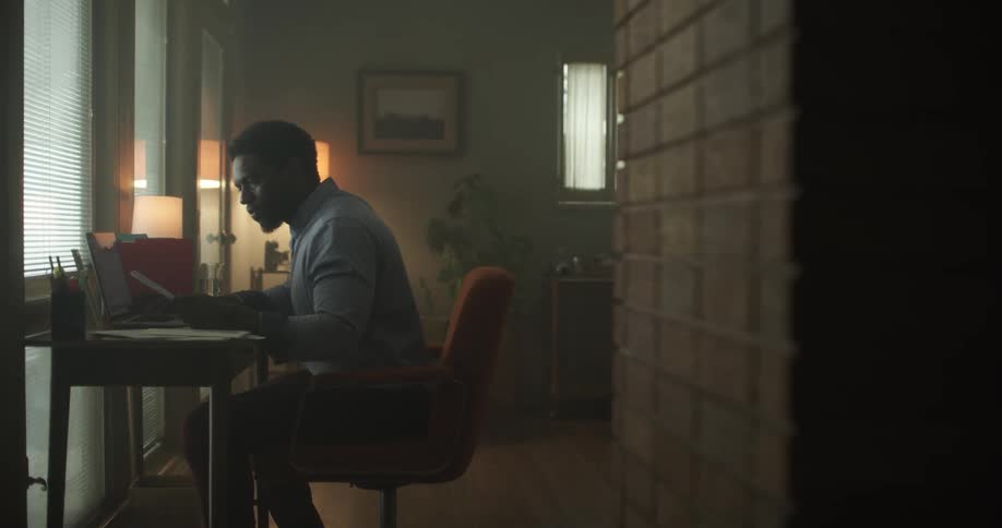 A man sitting at his desk with his laptop looks at his phone
