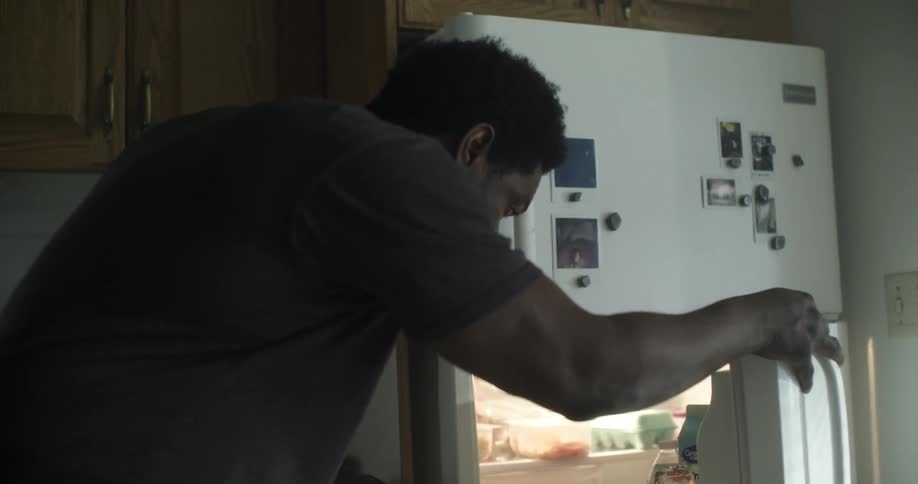 A man is grabbing a water bottle from a fridge