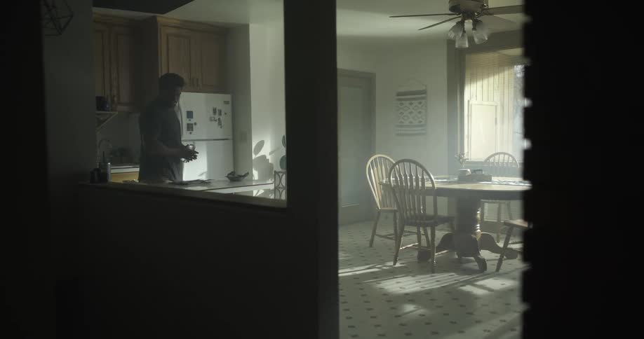 A man grabs a bottle of water from his refrigerator and walks away