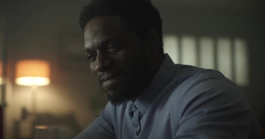 A black man sits inside a room smiling and nodding his head