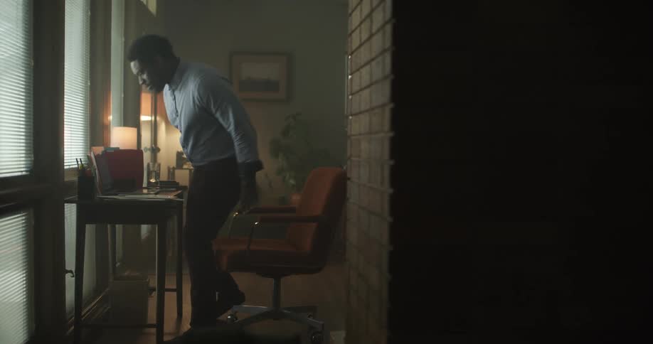 A man walks to his desk puts a glass of water down and sits down