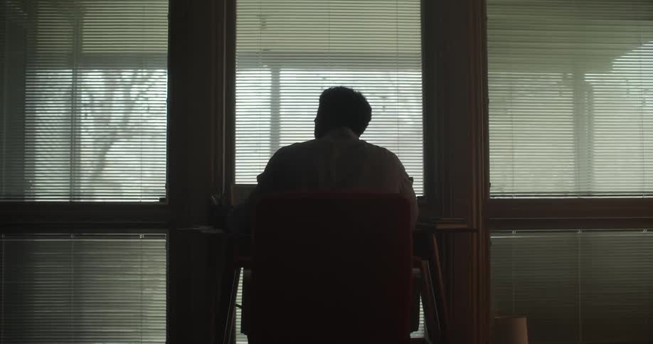 Silhouette of a man sitting at the desk in a dimly lit office