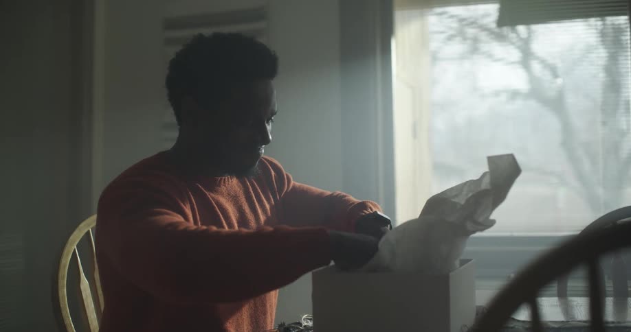 A black man opens a box and takes a robe out of it