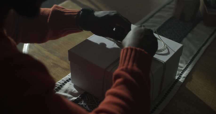 A man sitting a package at a table before sitting in a chair and beginning to untie the string that binds the package