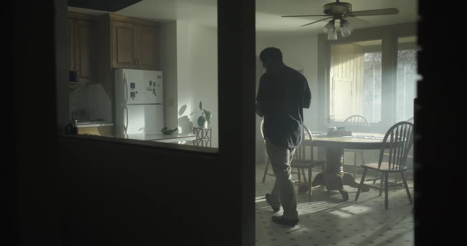 A man walking through a kitchen reading from a sheet of paper