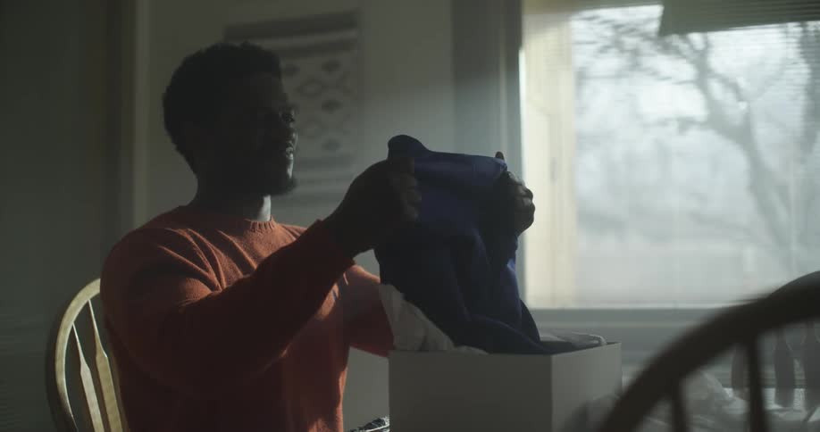 A man lifting a shirt from a box and smiling upon seeing what it is