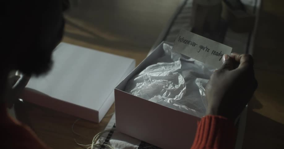 A man sitting at a dining room table opens a gift box and reads the enclosed note