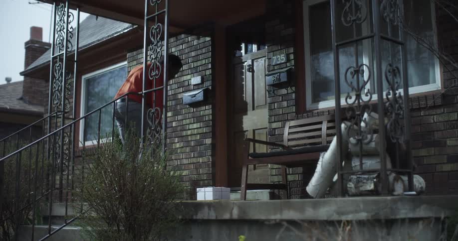 A man jogs up a few steps to the front porch of a home and picks up a package