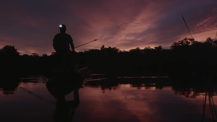 A man with a light on his helmet paddles a boat down a river