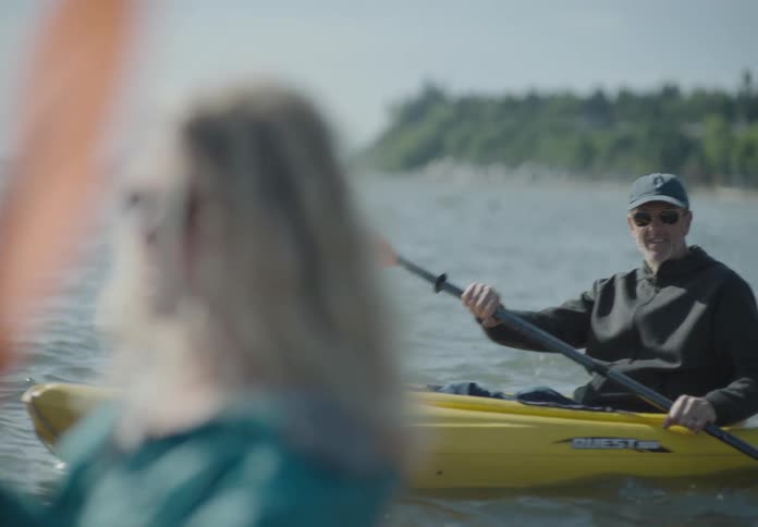 A white woman and white man paddle in kayaks in the ocean