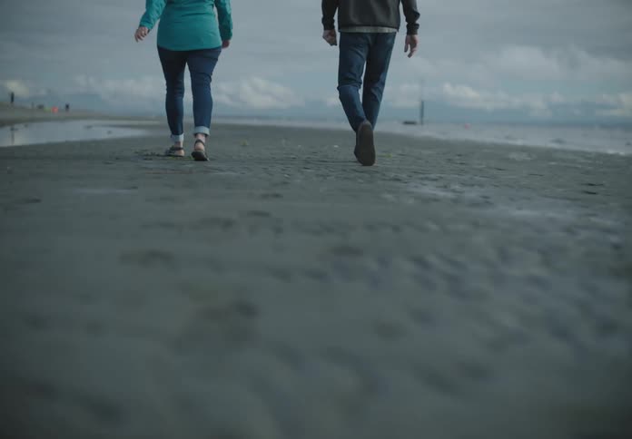 A man and a woman walk over a beach covered in water puddles on an overcast day