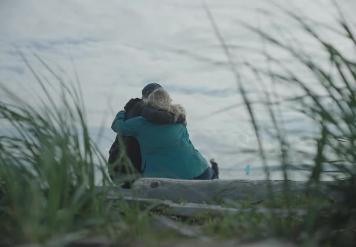 A white couple sits on a beach and hugs