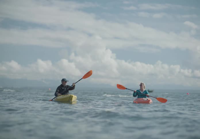 A white couple paddle kayaks in the ocean