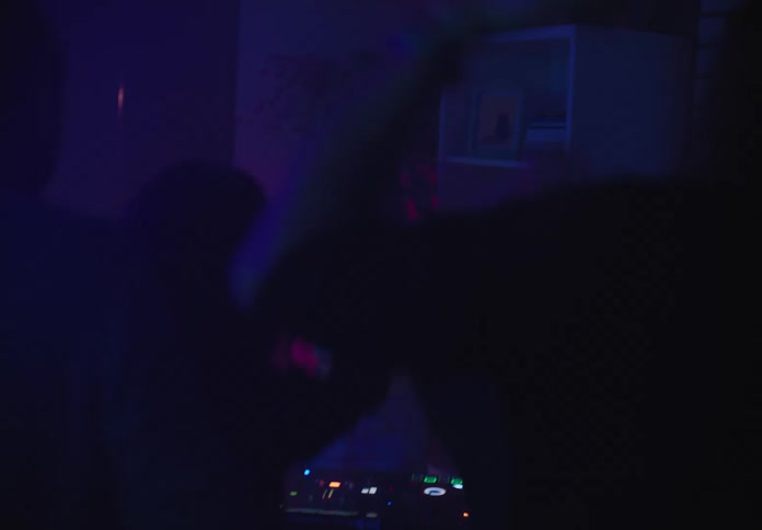 A female dj at a house party gets the crowd going while colorful lights flash