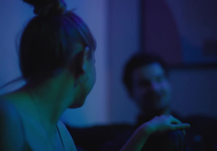 A white man and woman sit in a night club and talk