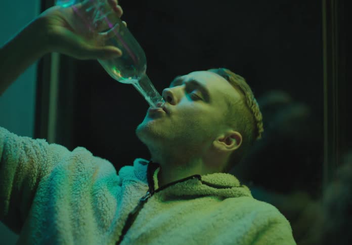 A man in a party drinking down a bottle of alcohol as others chair him