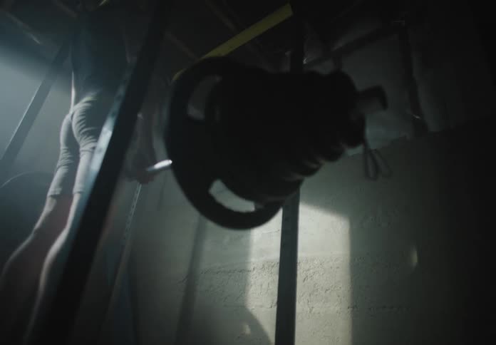 A white male lifts a weight bar loaded with weights in a basement