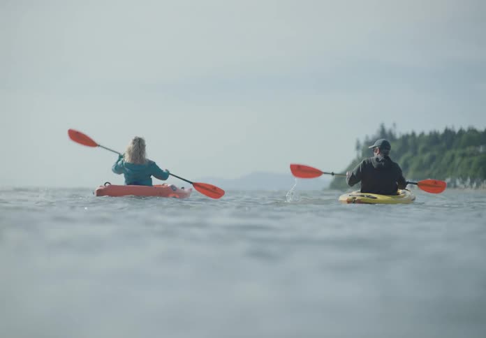 A man and a woman on a lake paddling kayaks