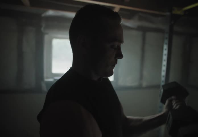 Male lifting heavy hand dumbbells in the basement of a house as the sunlight lights up the room