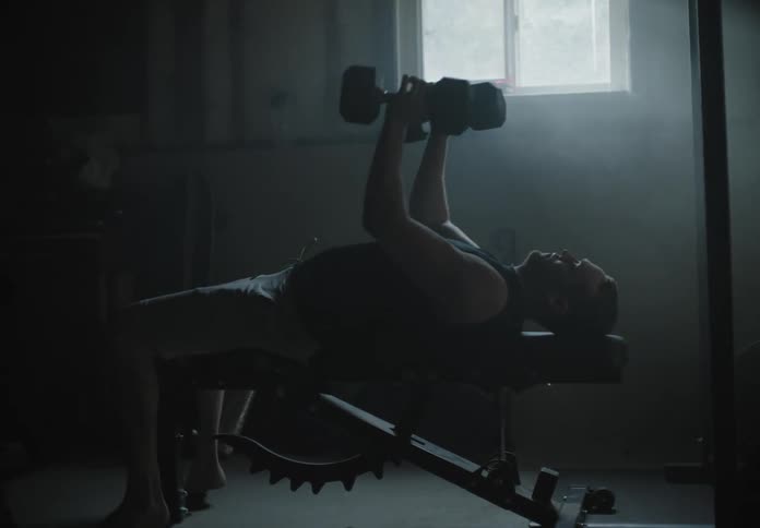 A man pick up a set of dumbbells and lies back on a weight bench to lift