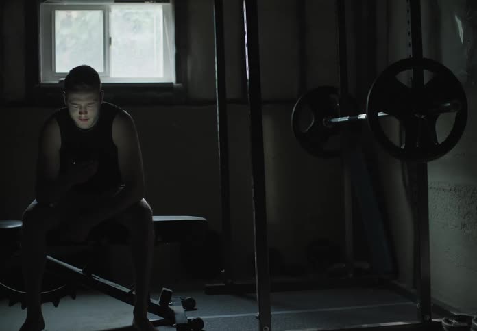 A man sitting on a workout bench video chatting on a smart phone