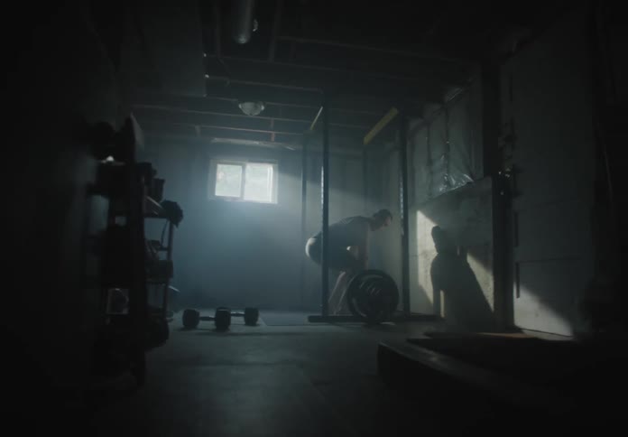 A white man lifts weights in the basement of a house