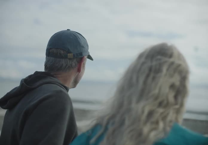 A white couple sit on the beach and hug and laugh