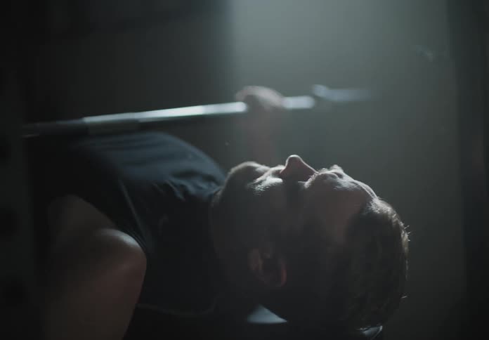A white man bench presses weights in the basement of a house