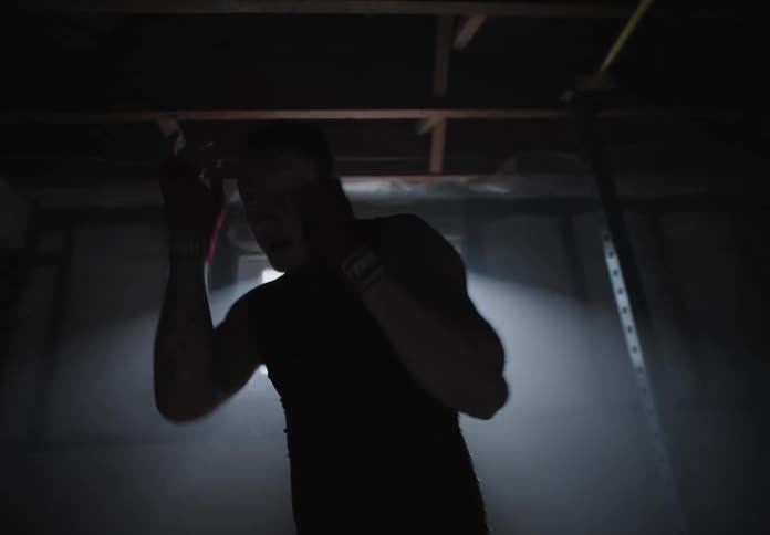 A man practices boxing moves in a dark basement