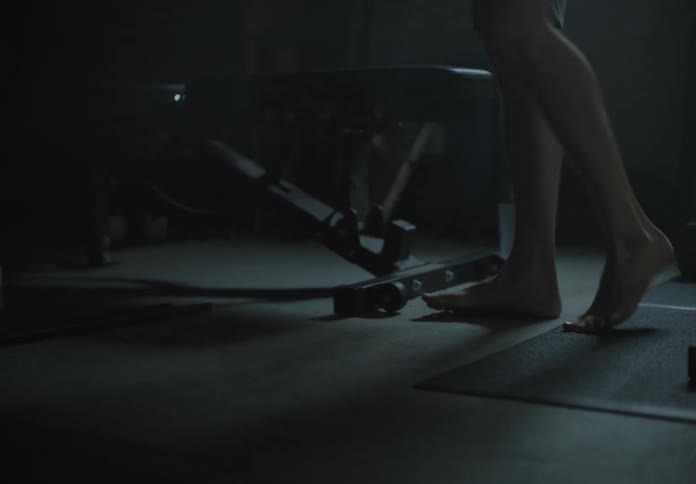 A white man fiddles with and moves a weight bench in a basement