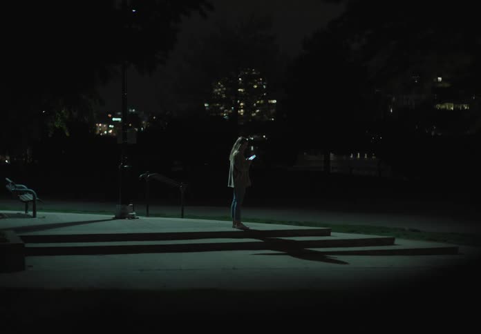 A white woman stands still in a dark park at night