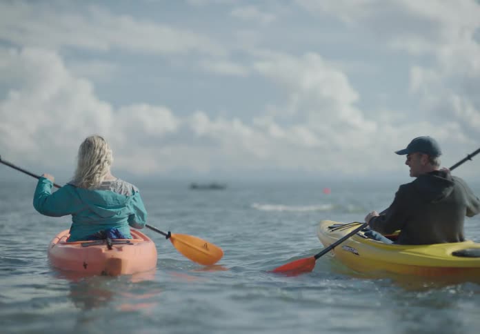 A man and woman turn oars in the ocean while sitting in two small canoes