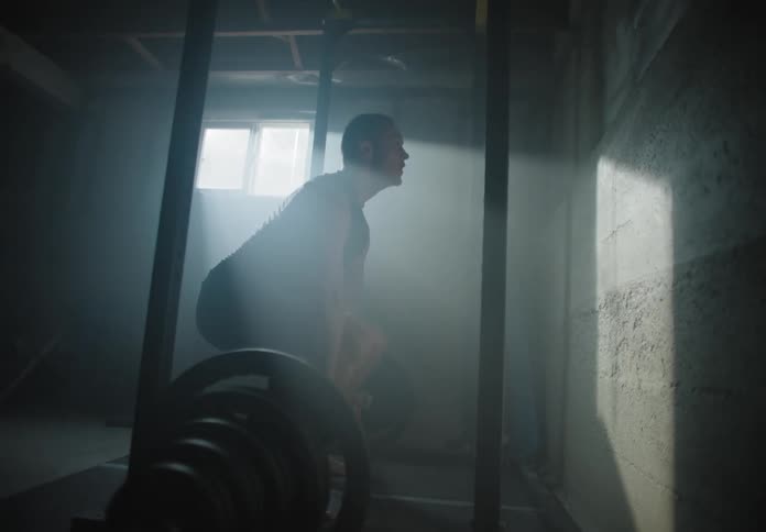 A white man lifts weights in the basement of a home