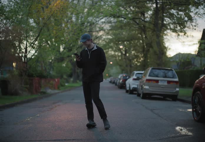 A man walks on a neighborhood road talking on a phone and looks back