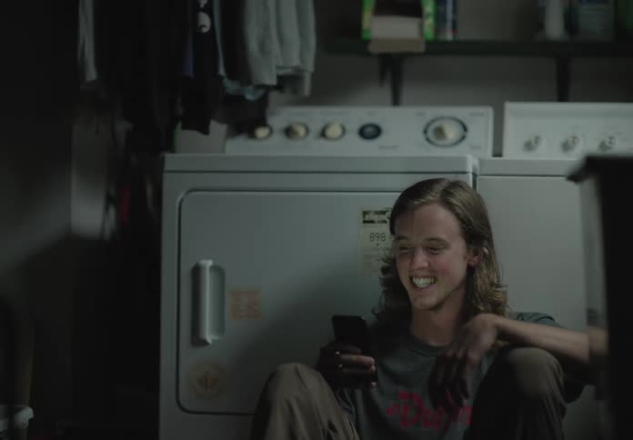 A man sitting down on the floor in the laundry room video chatting on a smart phone