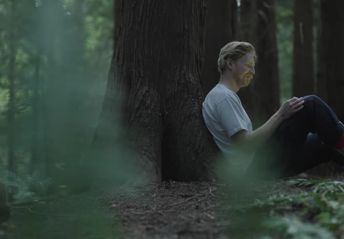 A man is sitting on the ground next to a tree