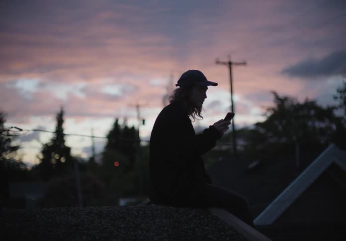 A man sitting on a roof video chatting on a smart phone
