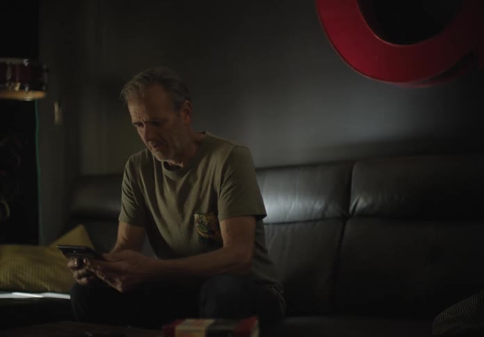 A man sits down on a couch and smiles as she looks at a tablet