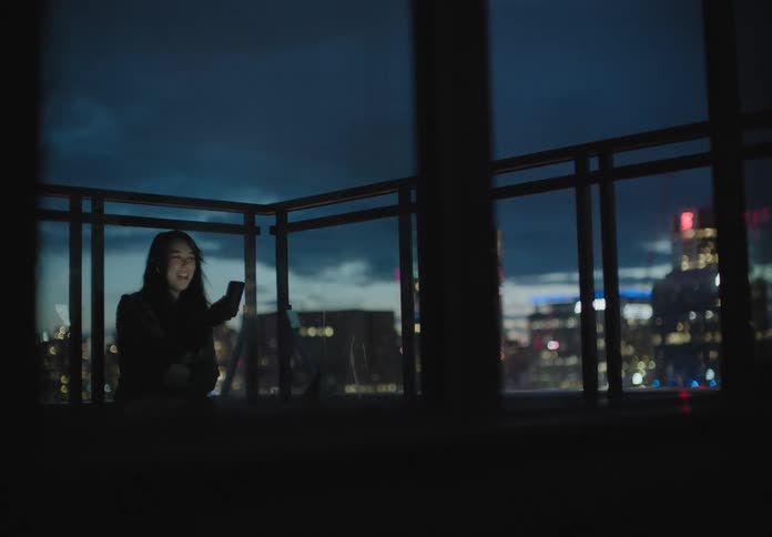 An asian woman in a room laughing while communicating via smartphone