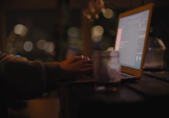 Female working on her laptop at night covers her mouth as she begins to yawn