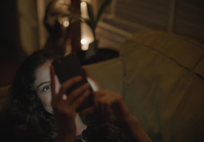A white woman reclines on a couch while talking on a smartphone