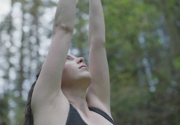 A woman stretching while standing on a grassy field with trees in the background