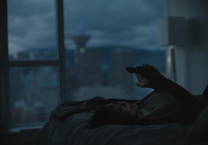 A white woman lies in bed talking on a smartphone