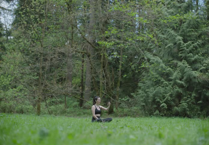 A woman sits alone in a large tree lined yard and picks up her cell phone