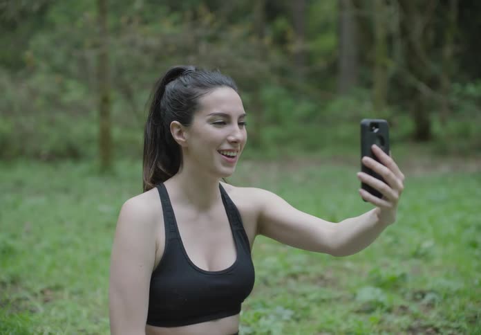 A woman sitting on grass video chatting on a smart phone