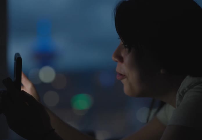 An asian teenager lies on a bed while talking on a smartphone